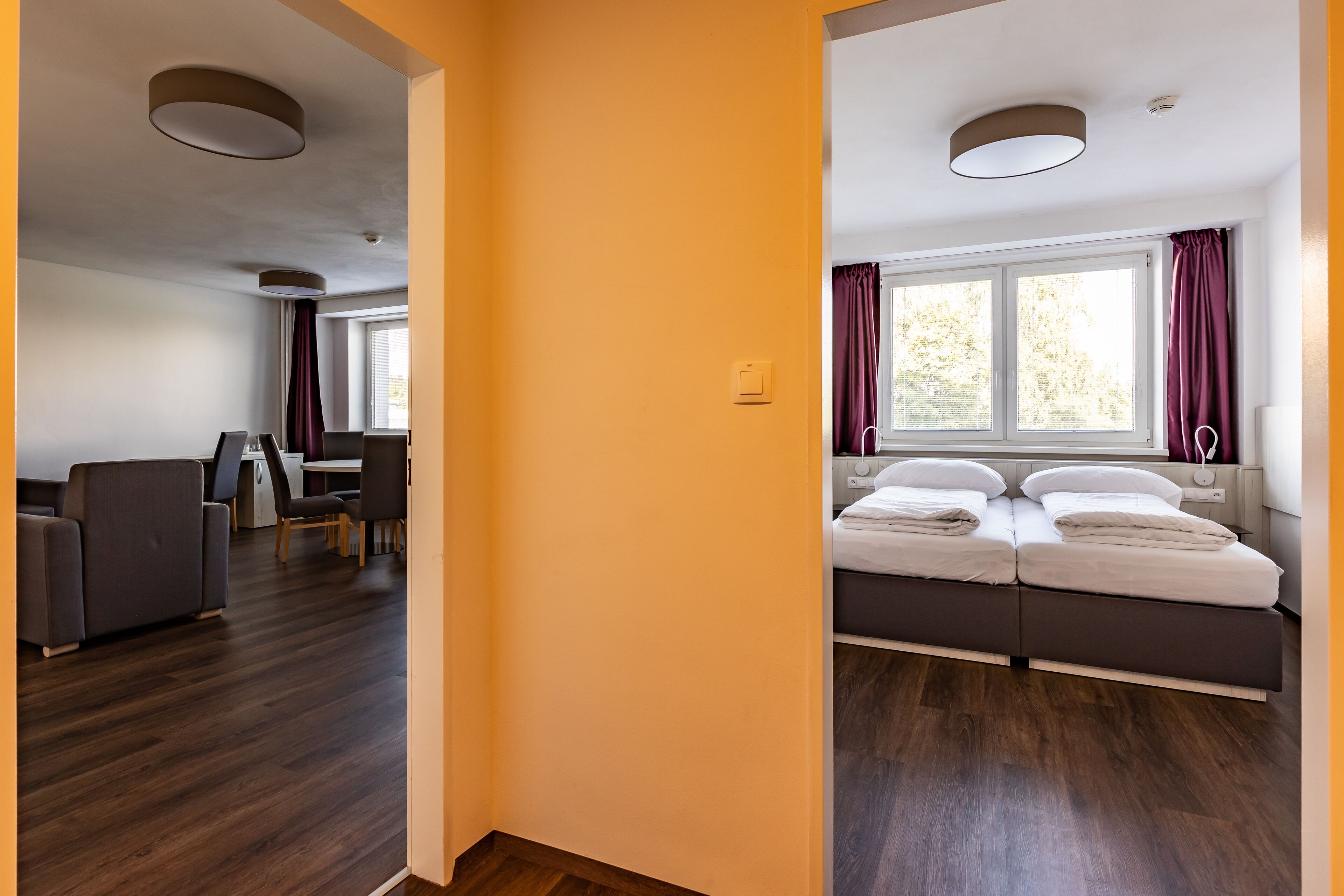 A modern hotel room with a bed, a desk, and a dining area.