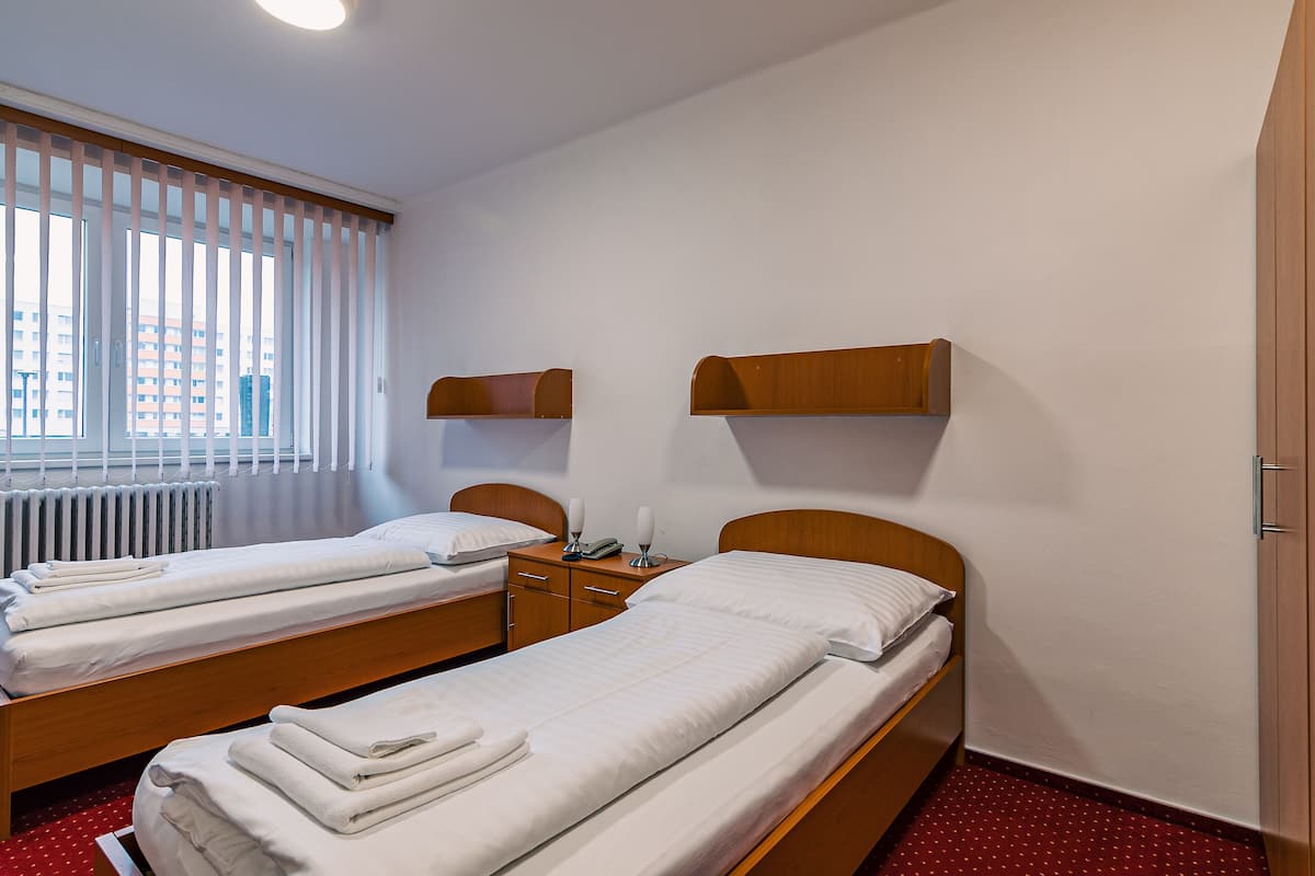A hotel room with two single beds, a wooden nightstand, a small table, and a window with blinds.