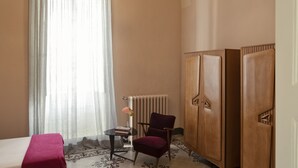 A hotel room with a bed, a small table with a book, a chair, a radiator, and a wooden wardrobe. - Calendula - Design apartment in historic building 5 min from Lecce (San Cesario di Lecce)
