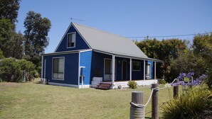 A blue house with a grey roof, a front porch, and a small garden with purple flowers.