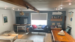 A cozy living room with a sofa, a coffee table, a wooden dining table, and a TV.