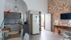 Une cuisine moderne avec un mur en pierre, un coin repas doté d’une table en verre et un téléviseur posé sur un meuble en bois.