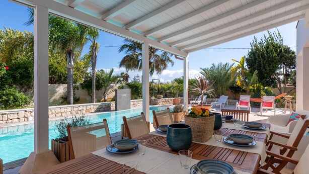 Un espace extérieur abrité, aménagé pour les repas, avec vue sur la piscine, des tables et des chaises en bois.