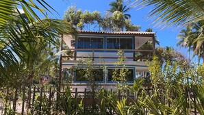 A two-story building with large windows and a balcony, surrounded by lush greenery and palm trees. - Glass lacquer! Jacuzzi on the sand with gourmet area! (BA)