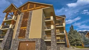 A multi-story building with a stone facade, multiple balconies, and a garage. - Sable Ridge View Suite -  Fireplace - Pool - A/C. (Radium Hot Springs)