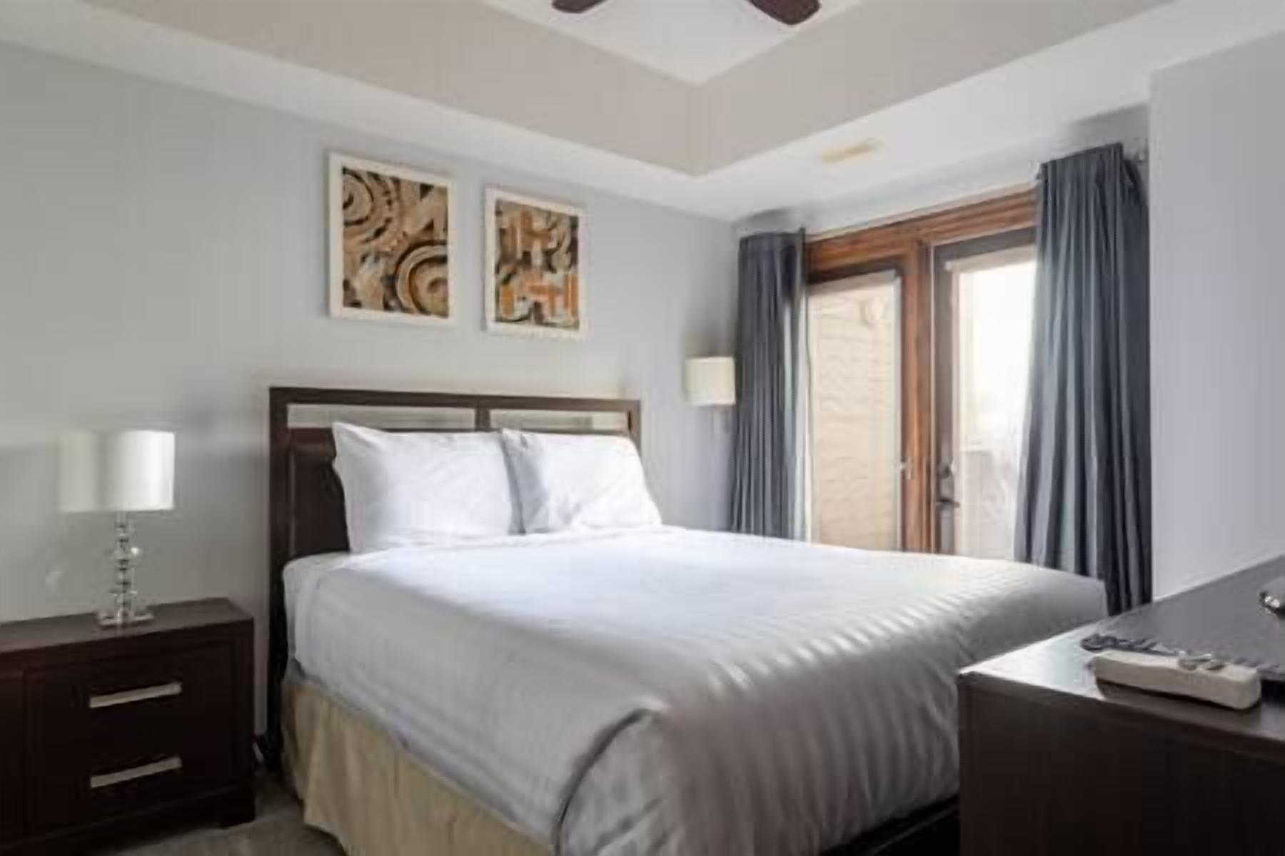 A hotel room with a bed, a nightstand, a desk, and a window with curtains.