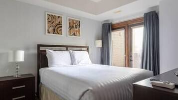 A hotel room with a bed, a nightstand, a desk, and a window with curtains.