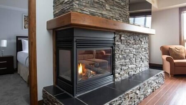 A modern living room with a stone fireplace, a wooden ceiling, and a stone accent wall. - Sable Ridge View Suite -  Fireplace - Pool - A/C. (Radium Hot Springs)