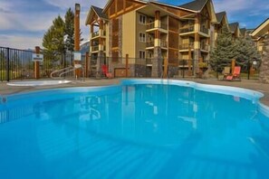 A swimming pool with a wooden deck and a multi-story building in the background. - Sable Ridge View Suite - Fireplace - Pool - A/C. (Radium Hot Springs)