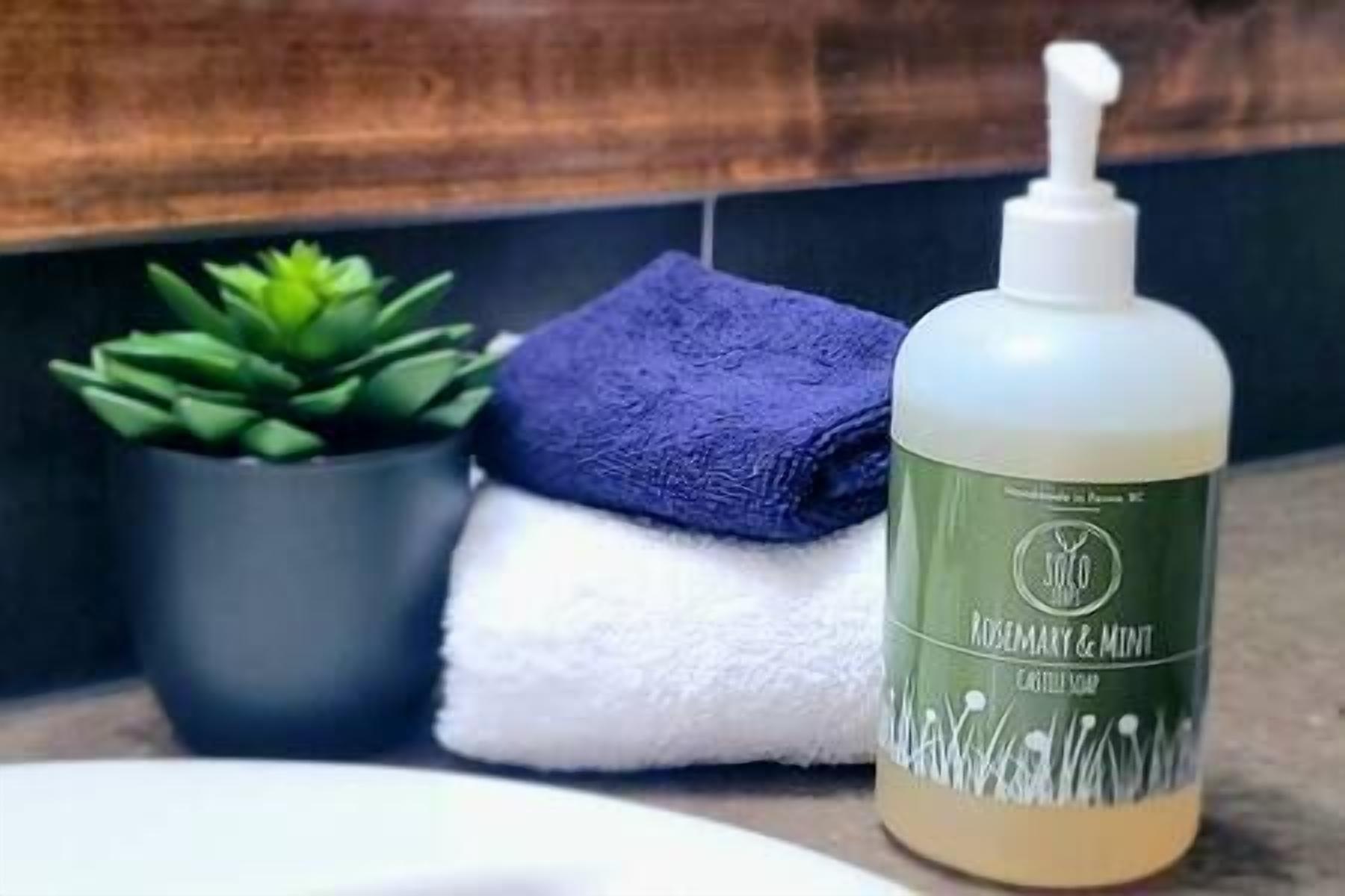 Un baño con una botella de jabón corporal de Romero y Menta, una toalla azul y una planta verde en maceta.