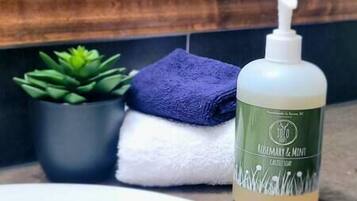 Un baño con una botella de jabón corporal de Romero y Menta, una toalla azul y una planta verde en maceta.