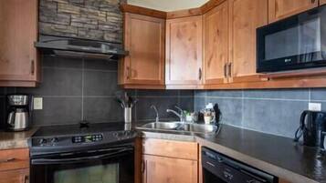 Una cocina con armarios de madera, salpicadero de piedra, estufa, microondas y lavavajillas.