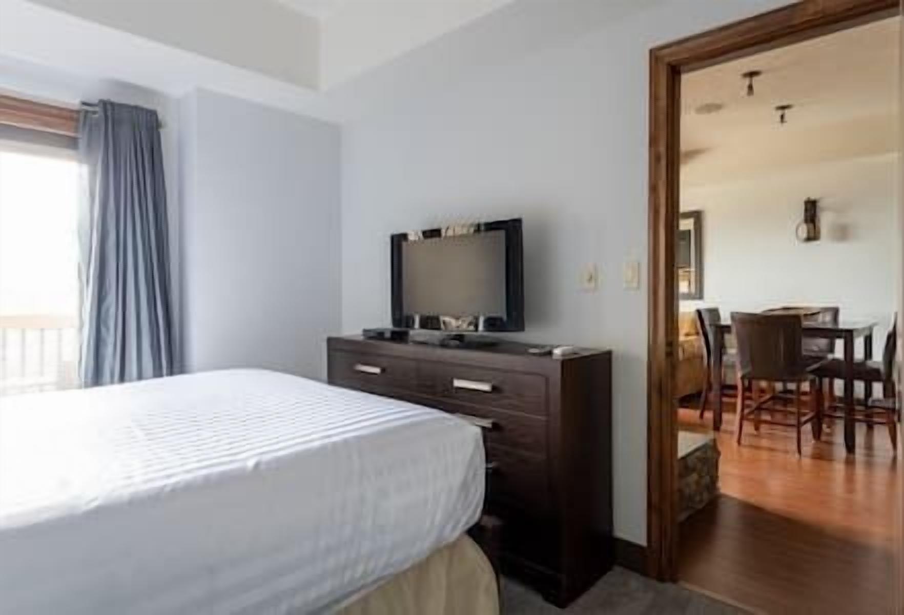 Une chambre d’hôtel avec un lit, un téléviseur posé sur une commode, un coin repas avec des chaises et un plancher en bois.