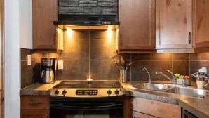 A kitchen with wooden cabinets, a stove, a coffee maker, and a sink. - Sable Ridge View Suite -  Fireplace - Pool - A/C. (Radium Hot Springs)