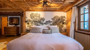 A cozy bedroom with a large bed, wooden ceiling, and a wall mural of trees. - Luxury Chalet in Courchevel with Pool, Hammam and Sauna (Courchevel 1850)