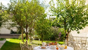 An outdoor dining area with a round table set for breakfast, surrounded by greenery and trees.