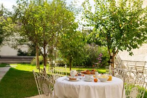 Un área de comedor al aire libre con una mesa redonda preparada para el desayuno, rodeada de follaje y árboles.