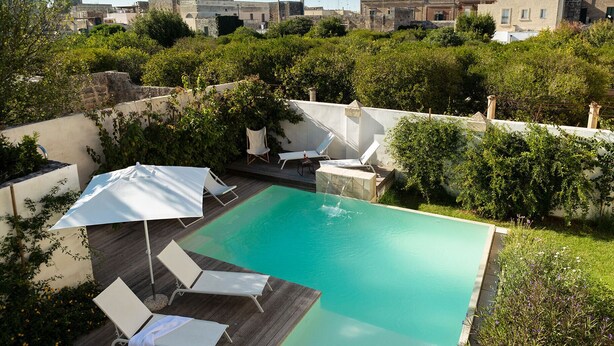 A rectangular swimming pool with a wooden deck and white lounge chairs.