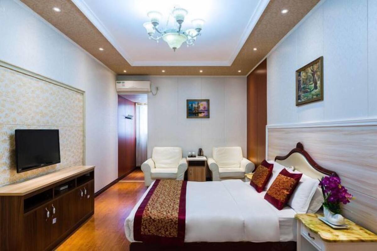 Habitación de hotel con cama, televisor, dos sillas, una mesita y un cuadro en la pared.