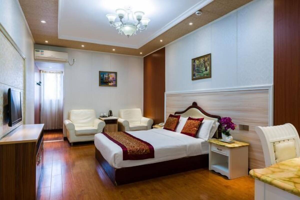 Una habitación de hotel con una cama grande, dos sillones, un televisor y una araña.