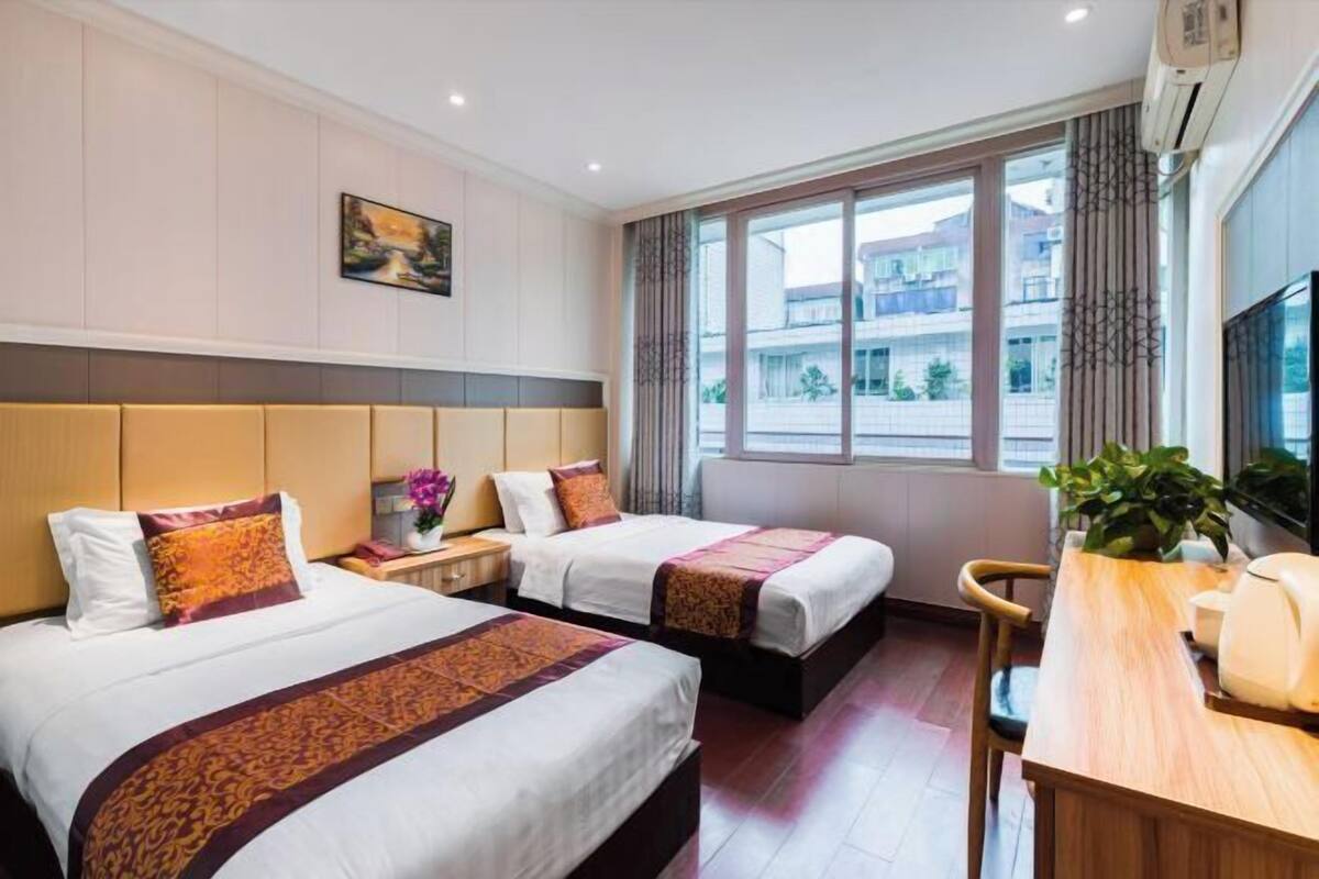 Habitación de hotel con dos camas, un escritorio y una ventana con vista a edificios.