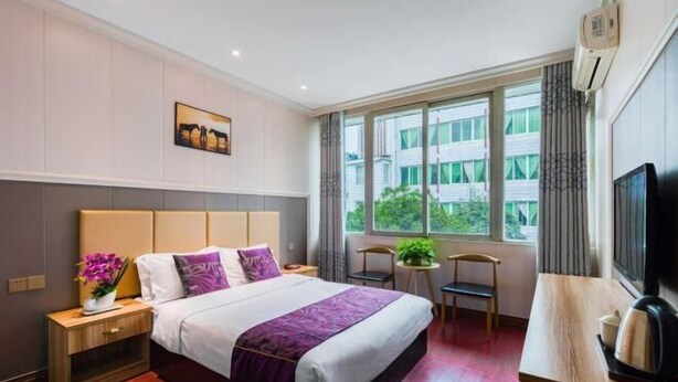 A hotel room with a bed, a desk, a television, and a window with a view of buildings. - Gongbaofu Hotel (Chongzhou)