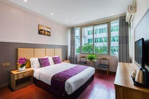 Habitación de hotel con cama, escritorio, televisión y ventana con vista a edificios.