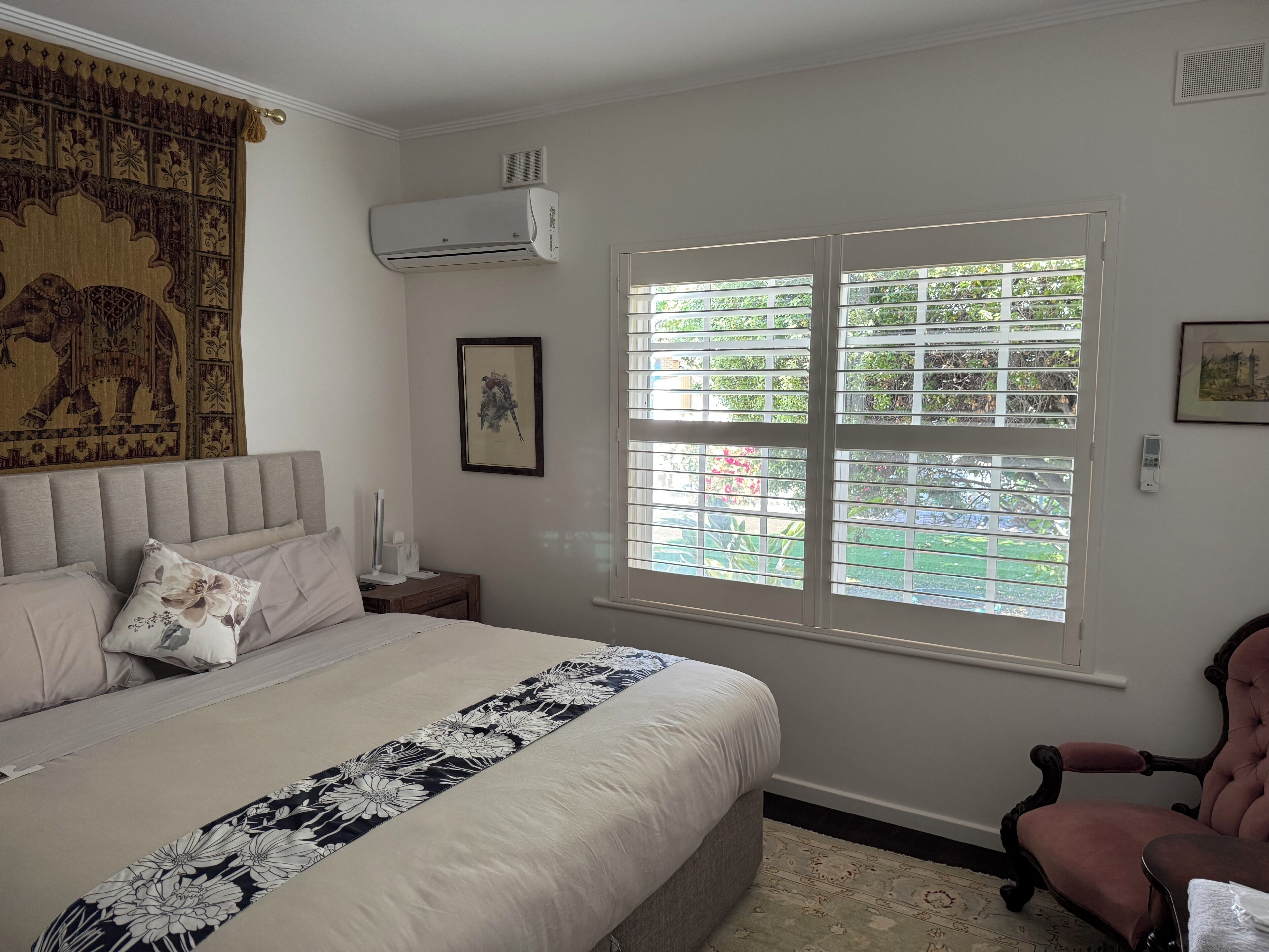 A bedroom with a bed, a nightstand, a chair, a window with blinds, and an air conditioning unit.