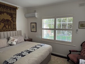 A bedroom with a bed, a nightstand, a chair, a window with blinds, and an air conditioning unit.