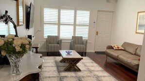 Una sala de estar con una mesa de centro de madera, sillas a rayas, un sofá color beige y una puerta blanca.