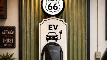 A wall-mounted electric vehicle charging station with a vintage Route 66 theme, including a sign that reads 'EV Get your Kicks' and a service sign stating 'SERVICE YOU CAN TRUST EST. 1926'.