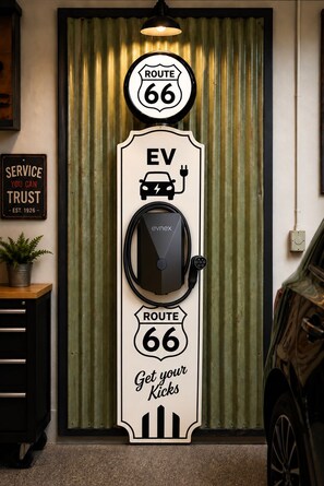 A wall-mounted electric vehicle charging station with a vintage Route 66 theme, including a sign that reads 'EV Get your Kicks' and a service sign stating 'SERVICE YOU CAN TRUST EST. 1926'.
