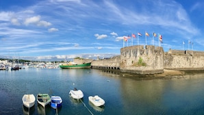 Un fort historique, orné de nombreux drapeaux, un port où sont amarrés de petits bateaux et un ciel d’un bleu limpide.