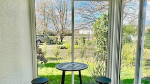 Une véranda avec une table et deux chaises, de grandes portes vitrées et une vue sur un jardin.