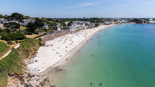 Une plage côtière avec un rivage sablonneux, une eau claire et un mélange de bâtiments résidentiels le long de la côte.