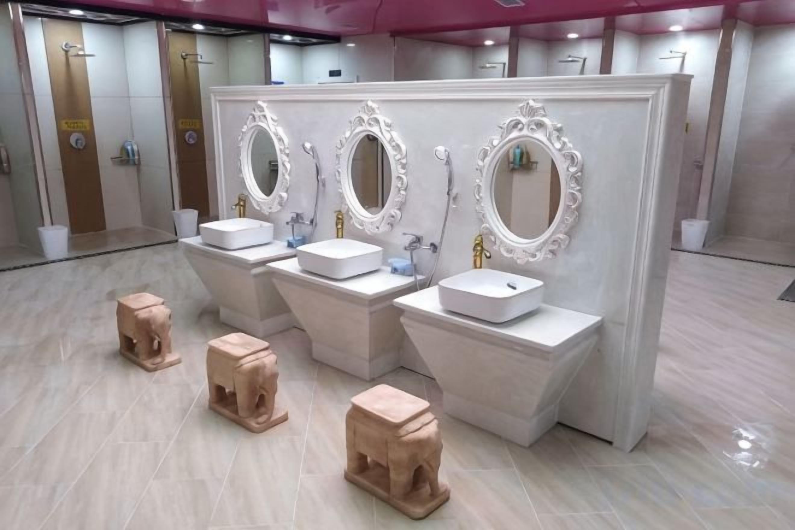 Baño con tres lavamanos, cada uno con espejo y dispensador de jabón.