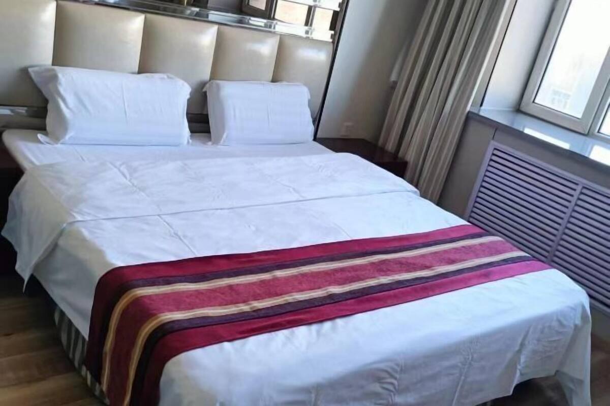 A hotel room with a bed, a headboard, a window, and a radiator.