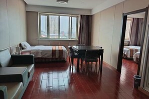 Ein Hotelzimmer mit Bett, Esstisch und Blick auf eine Stadtkulisse durch große Fenster.