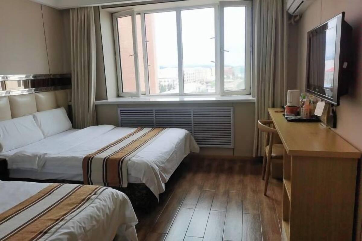 A hotel room with two beds, a desk, a chair, a TV, and a window with a city view.