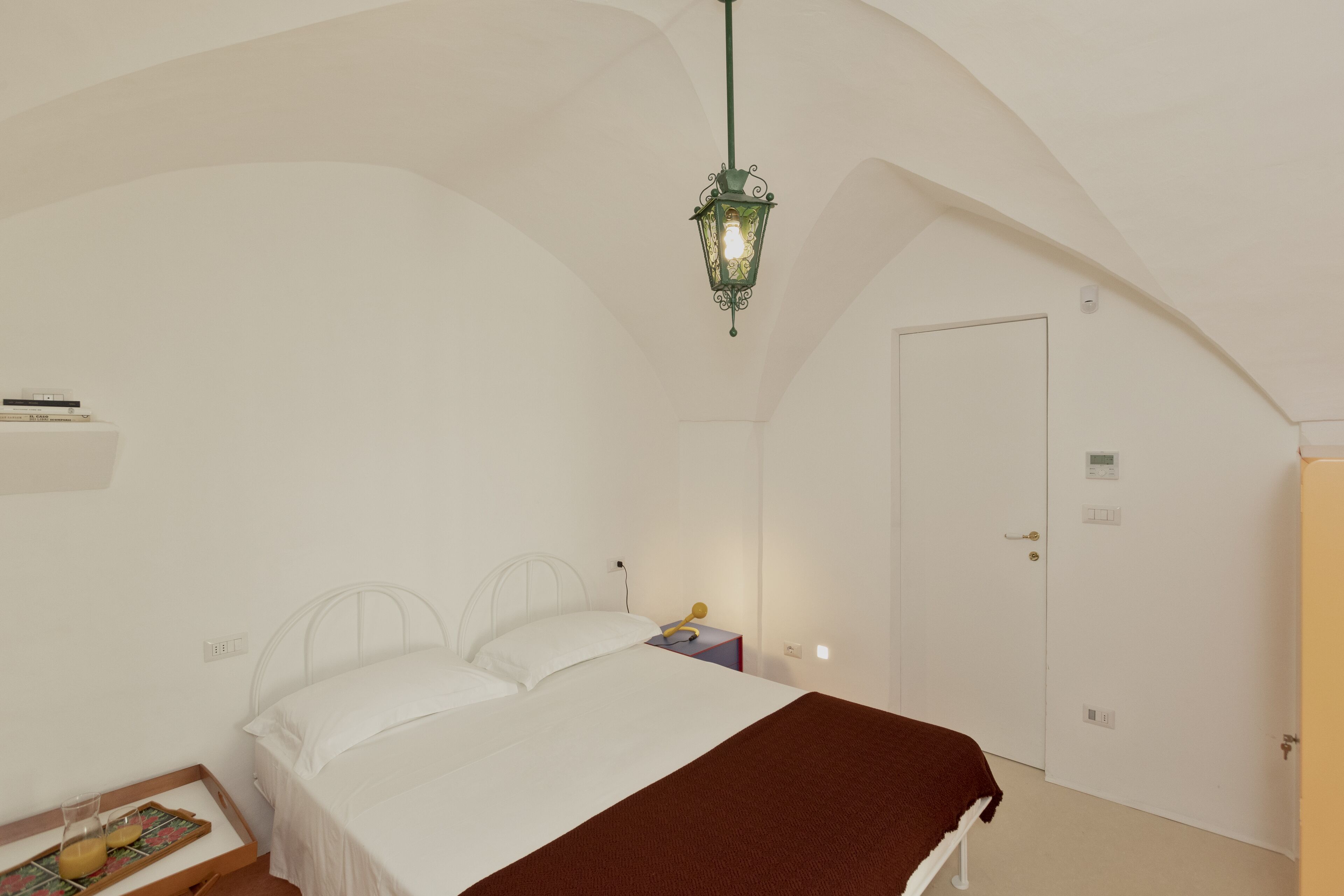 Una camera da letto con un letto, un comodino, una lampada e una porta.