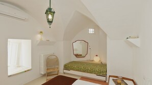 A bedroom with a sloped ceiling, a bed with a floral bedspread, a bedside table with a lamp, a window, and a radiator. - Laurel - Designer apartment in historic building 5 min from Lecce (San Cesario di Lecce)