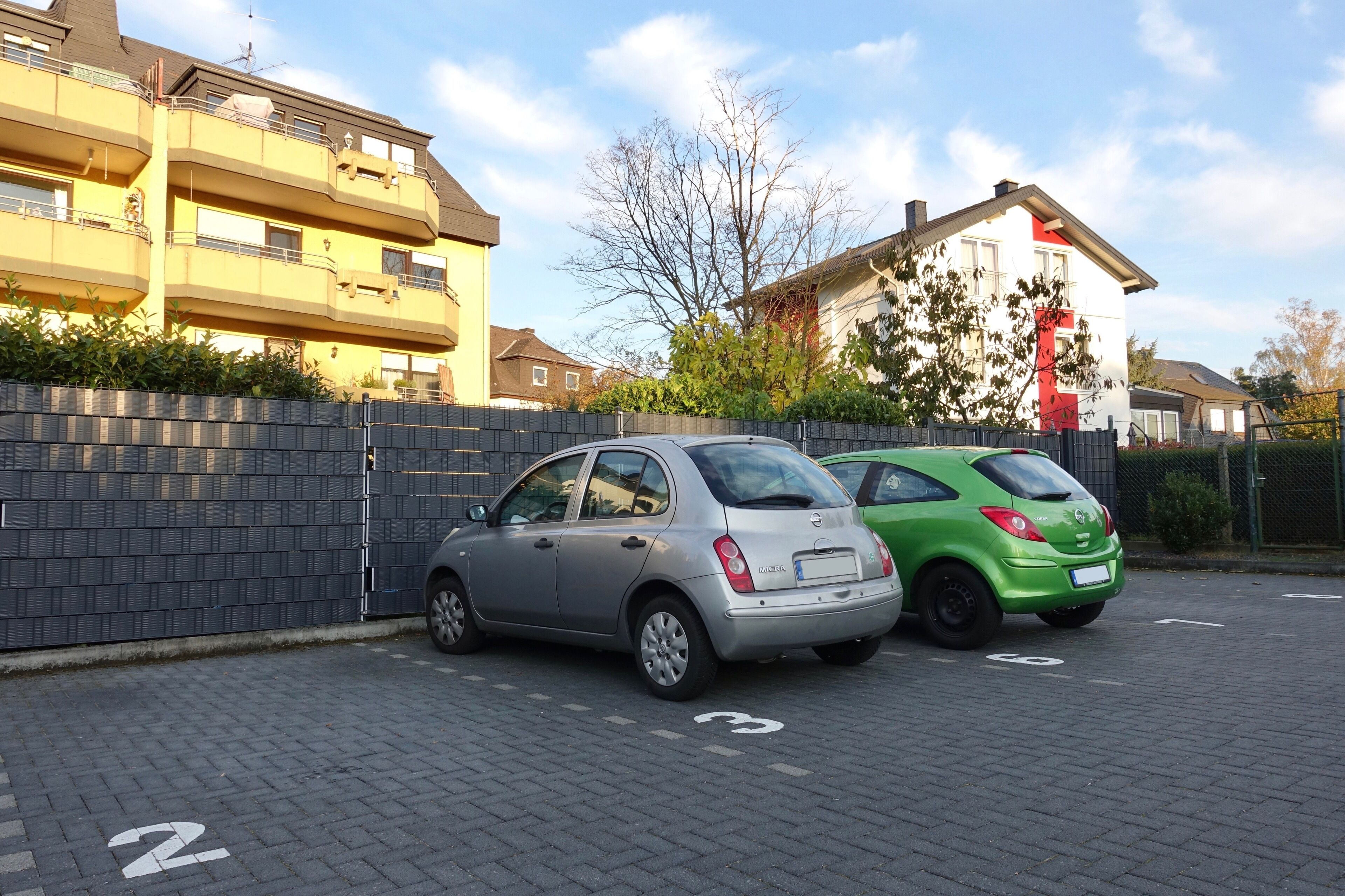 Zwei Autos auf einem befestigten Platz mit einer Backsteinmauer und einem Zaun.