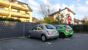 Zwei Autos auf einem befestigten Platz mit einer Backsteinmauer und einem Zaun.