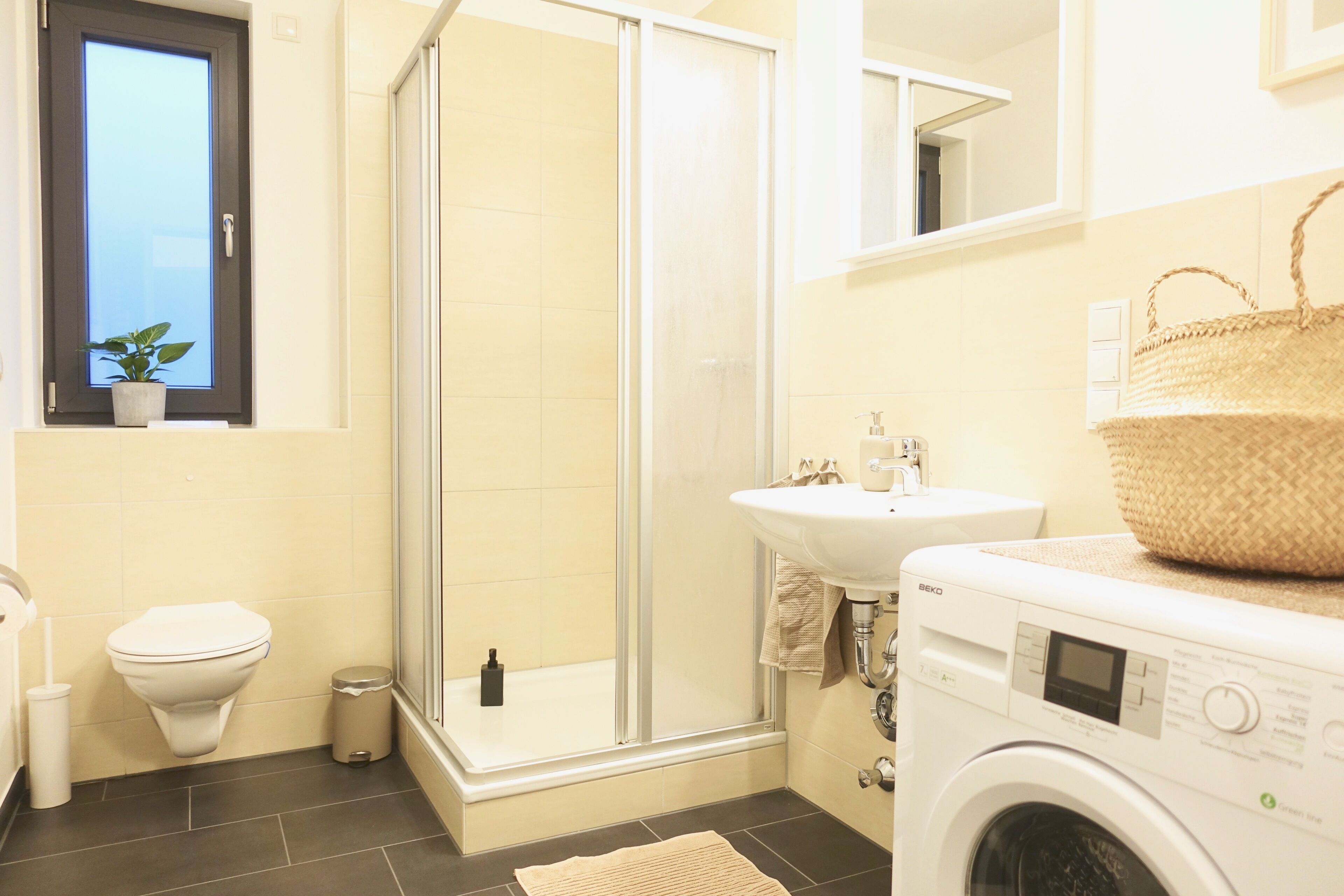 A bathroom with a toilet, a glass-enclosed shower, a sink, and a washing machine.