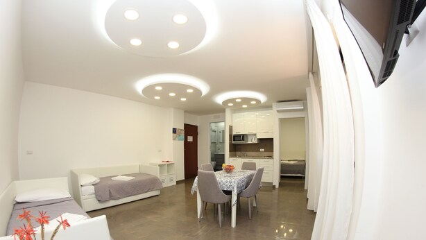 A modern, compact living space with a dining area, kitchenette, and a bed.