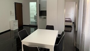 A modern, well-lit room with a white table and chairs, a small kitchenette, and a door leading to another room.