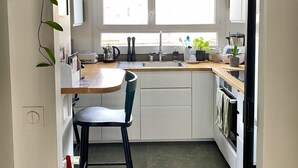 Cocina compacta con área de comedor, que incluye un ventanal, una planta colgante y una lámpara moderna.