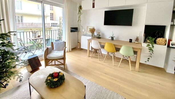 Una sala de estar moderna con una mesa de comedor de madera, sillas coloridas, un televisor montado en la pared y un balcón con vista al edificio.