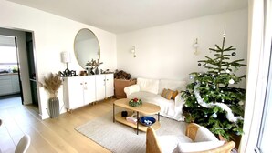 Una sala de estar moderna con un sofá blanco, una mesa de centro, un árbol de Navidad y un espejo grande.