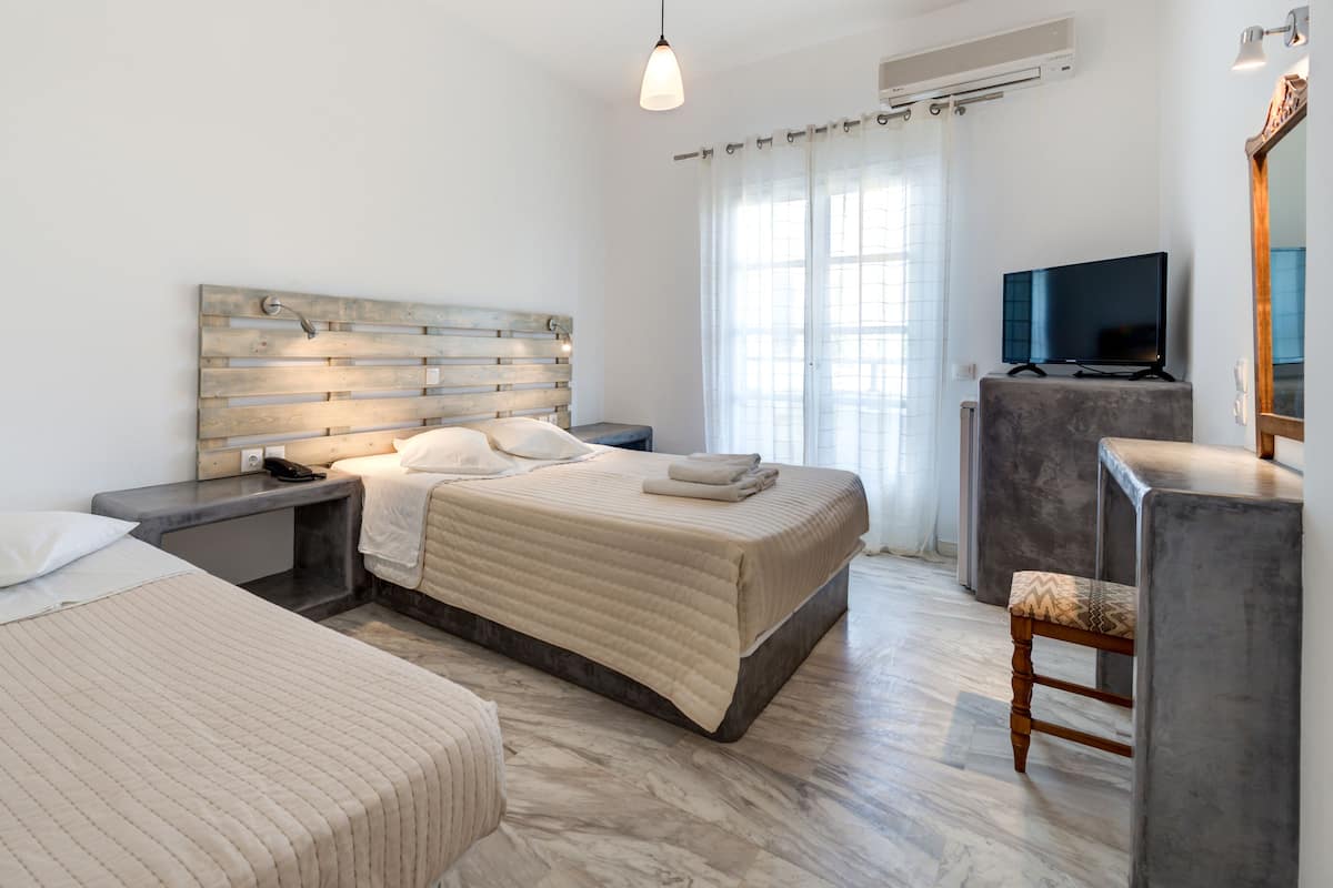 Une chambre d’hôtel moderne équipée de deux lits, d’un bureau, d’une télévision et d’une grande fenêtre avec des rideaux.